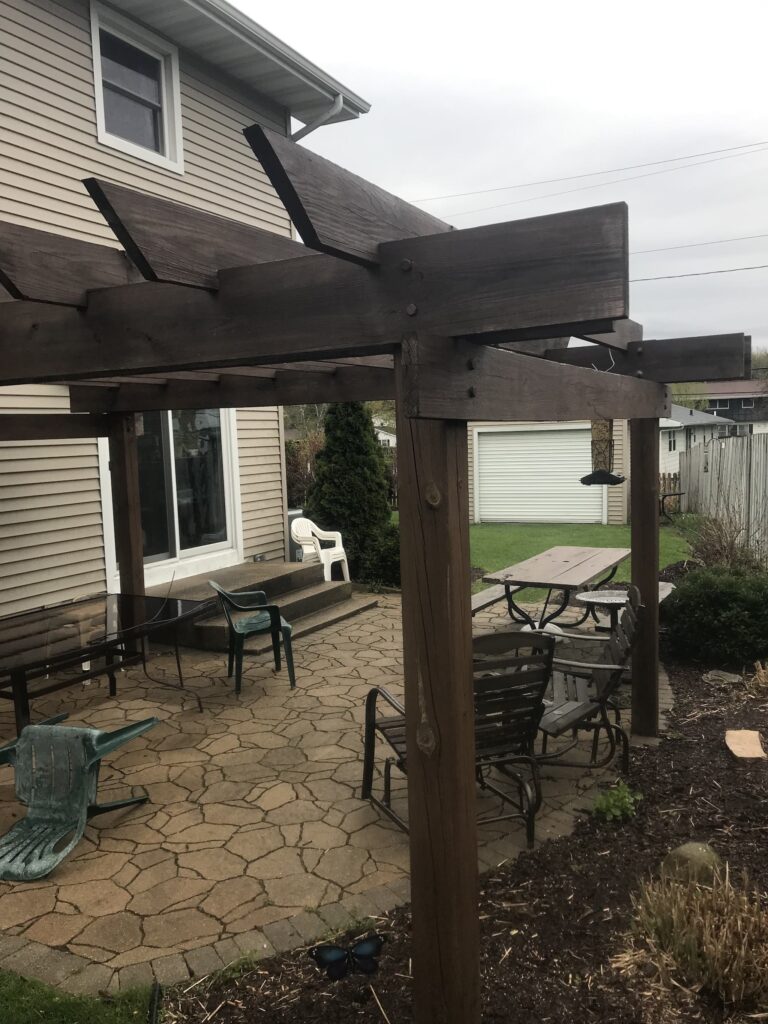 Wooden pergola over a backyard patio with furniture.